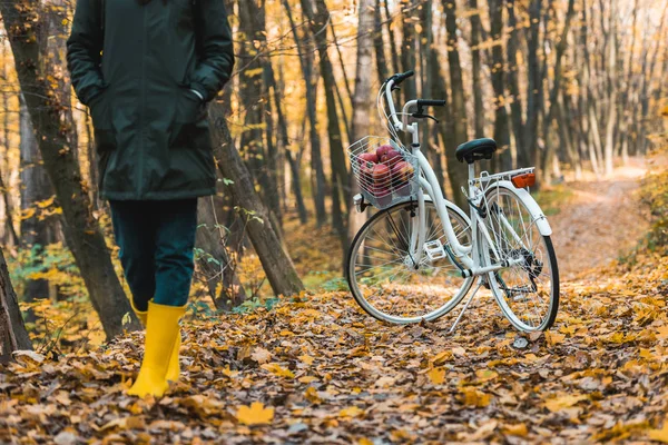 Image recadrée de la femme en bottes de gomme jaune marchant près du vélo dans la forêt automnale — Photo de stock