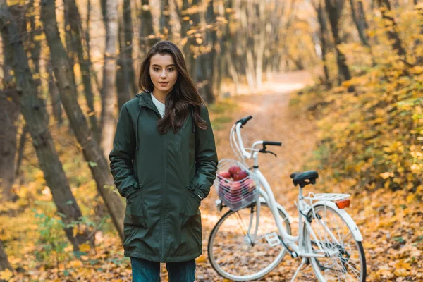 Beautiful young woman walking near bicycle in autumnal forest — Stock Photo