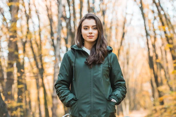 Bela jovem mulher no casaco olhando para a câmera na floresta outonal — Fotografia de Stock