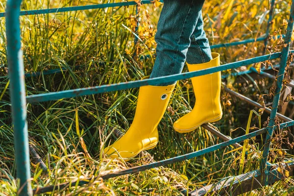 Seção baixa de mulher em botas de borracha amarela andando sobre trilhos ao ar livre — Fotografia de Stock