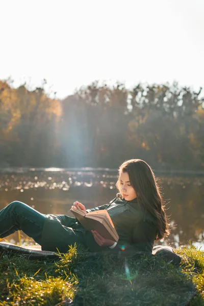 Attrayant fille étendu sur couverture et livre de lecture près de l'étang dans le parc — Photo de stock