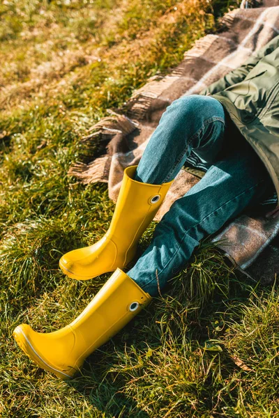 Imagen recortada de la mujer en botas de goma amarillas que ponen en la manta al aire libre - foto de stock