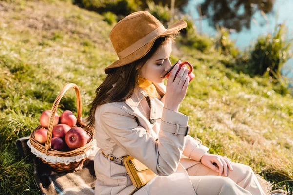 Foco seletivo da jovem mulher elegante em chapéu e casaco de trincheira beber café ao ar livre — Fotografia de Stock