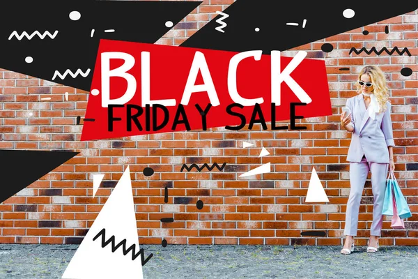Stylish young woman with shopping bags using smartphone while standing in front of brick wall, black friday sale banner — Stock Photo