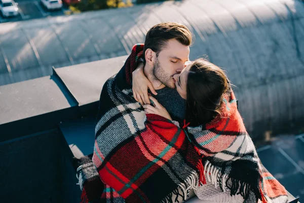 Vista ad alto angolo di bella giovane coppia coperta di plaid baciare sul tetto — Foto stock