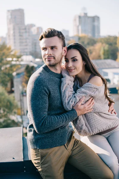 Belo jovem casal abraçando no telhado e olhando em algum lugar — Fotografia de Stock