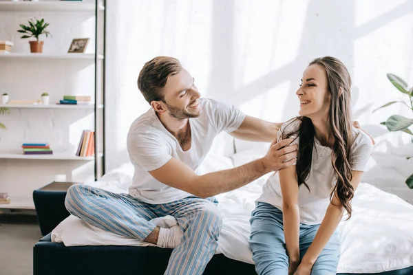 Riendo pareja joven divirtiéndose mientras se sienta en la cama por la mañana - foto de stock