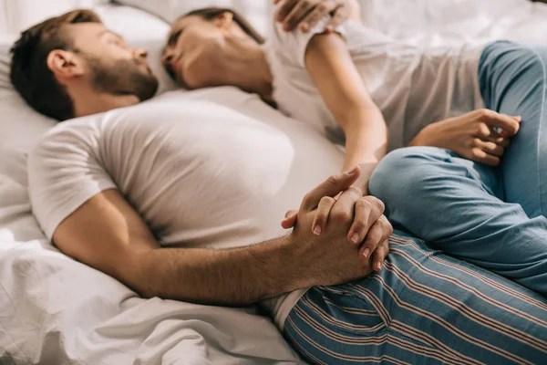 Jovem casal de pijama de mãos dadas na cama de manhã — Fotografia de Stock