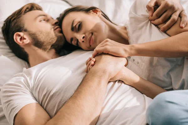 Hermosa pareja joven en pijama de la mano en la cama por la mañana - foto de stock