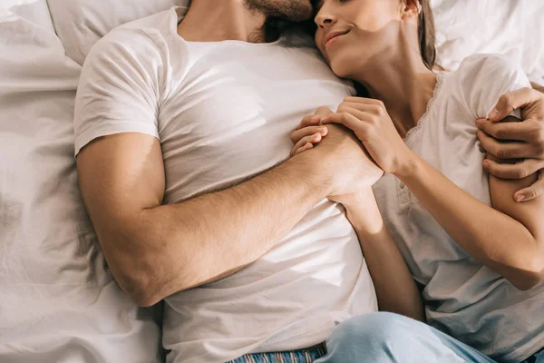 Обрезанный снимок молодой пары в пижаме, обнимающейся в постели утром — стоковое фото