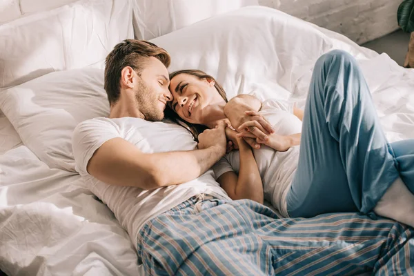 Beautiful young couple in pajamas cuddling in bed in morning — Stock Photo