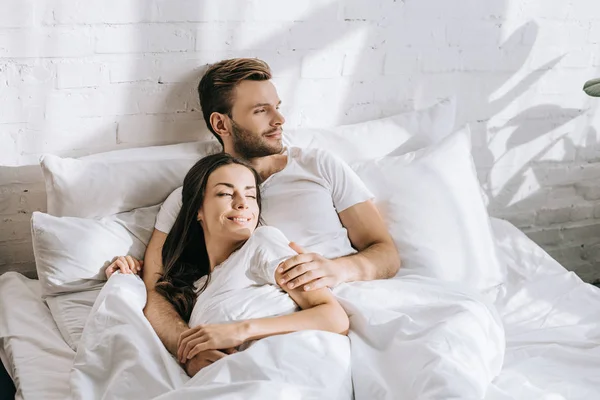 Hansdome junger Mann entspannt sich morgens im Bett mit seiner schlafenden Freundin — Stockfoto