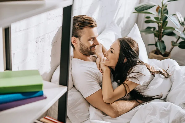 Glückliches junges Paar entspannt sich und plaudert morgens im Bett — Stockfoto