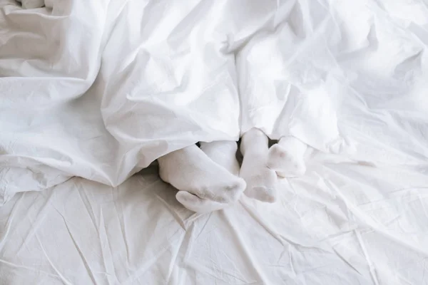 Plan recadré de couple en chaussettes blanches se détendre au lit sous la couverture — Photo de stock