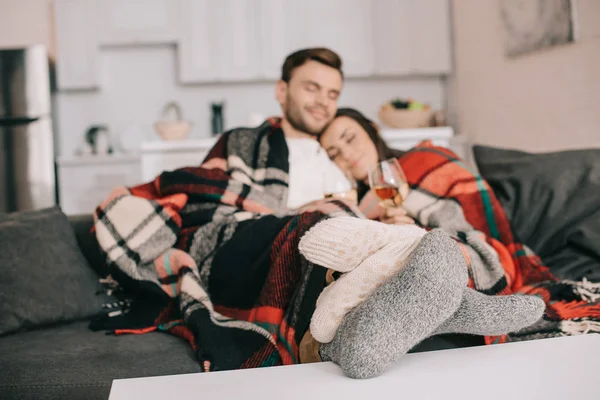 Glückliches junges Paar mit Gläsern Weißwein entspannt auf der Couch unter karierten — Stockfoto
