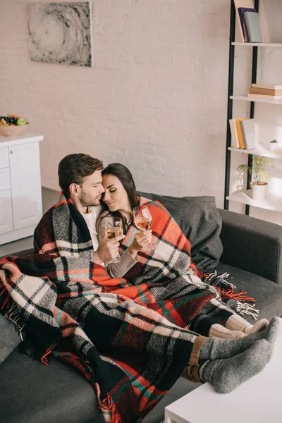 High angle view of beautiful young couple with glasses of white wine relaxing on couch under plaid — Stock Photo
