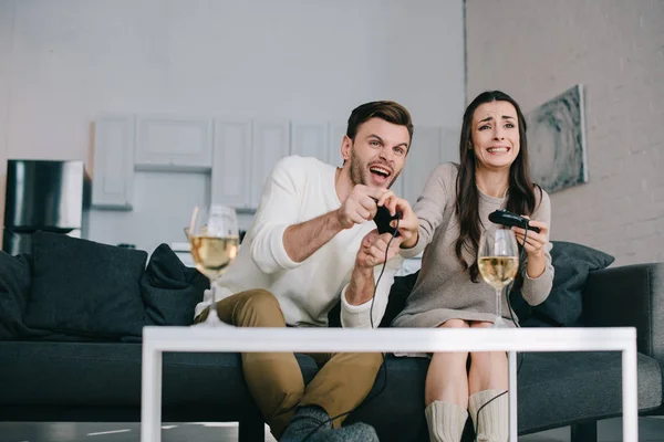 Jeune couple expressif jouant jeu vidéo rétro sur le canapé à la maison — Photo de stock