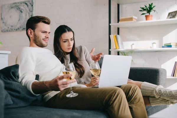 Красива молода пара використовує ноутбук і п'є вино разом на дивані вдома — стокове фото