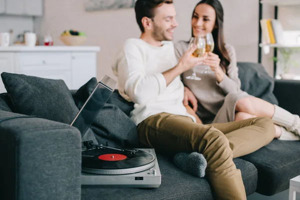 Happy young couple listening music with vinyl record player and drinking wine at home — Stock Photo