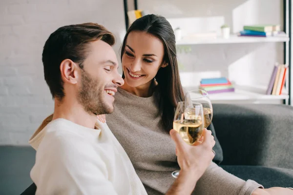 Hermosa joven pareja bebiendo vino en el sofá en casa - foto de stock