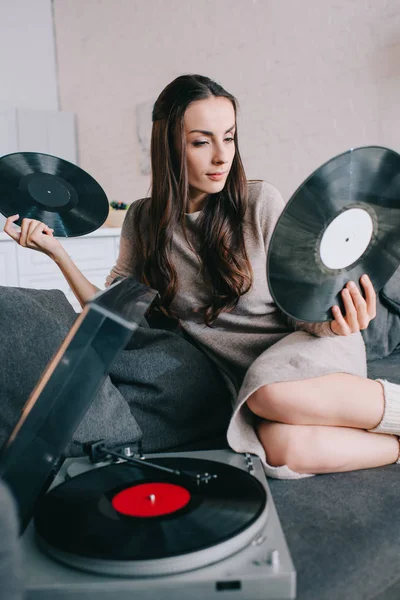 Beautiful young woman holding discs for vinyl record player on couch at home — Stock Photo