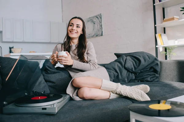 Beautiful young woman listening music with vinyl record player on couch at home — Stock Photo