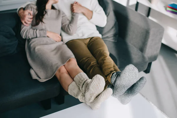 Tiro recortado de pareja en calcetines de lana caliente relajarse en el sofá en casa - foto de stock