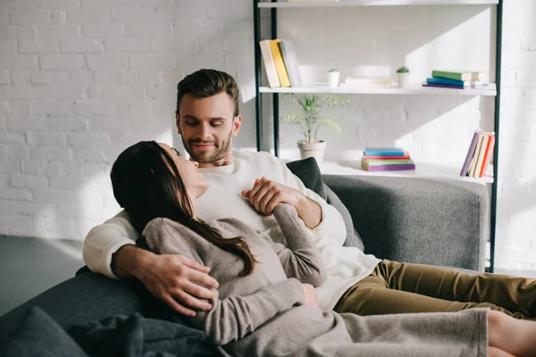 Happy young couple relaxing on couch and holding hands at home — Stock Photo