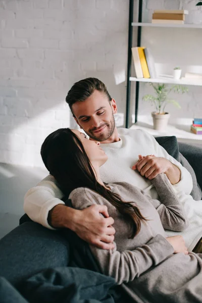 Hermosa pareja joven relajarse en el sofá y tomarse de la mano en casa — Stock Photo