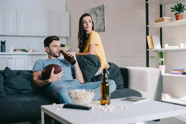 Sorrindo jovem casal assistindo jogo de futebol americano em casa — Fotografia de Stock