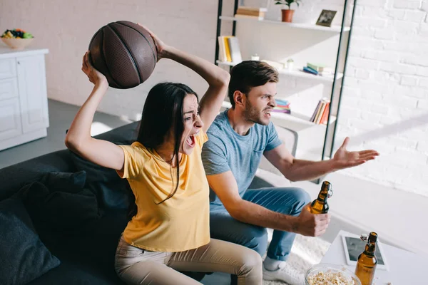 Visão de alto ângulo de jovem casal emocional com cerveja torcendo para o jogo de basquete em casa — Fotografia de Stock