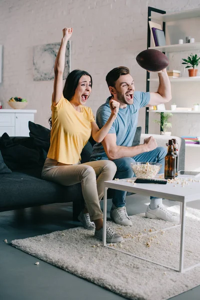 Emocional pareja joven animando para el partido de fútbol americano en casa — Stock Photo