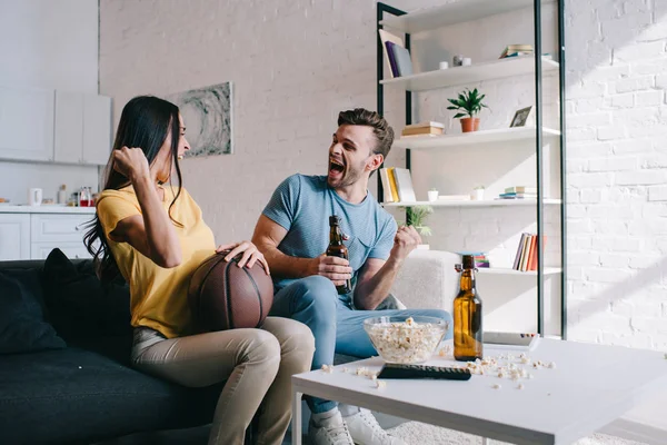 Jovem casal emocional com cerveja torcendo para o jogo de basquete em casa — Fotografia de Stock