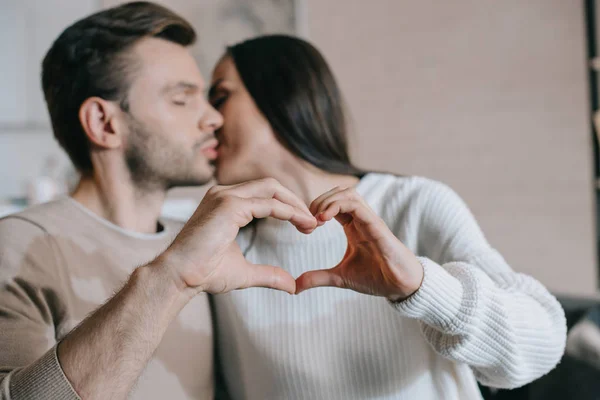 Hermosa pareja joven besando y haciendo símbolo del corazón con las manos - foto de stock