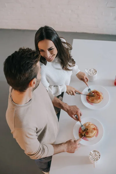 Vue grand angle de couple heureux avec crêpes et cacao pour le petit déjeuner à la maison — Photo de stock