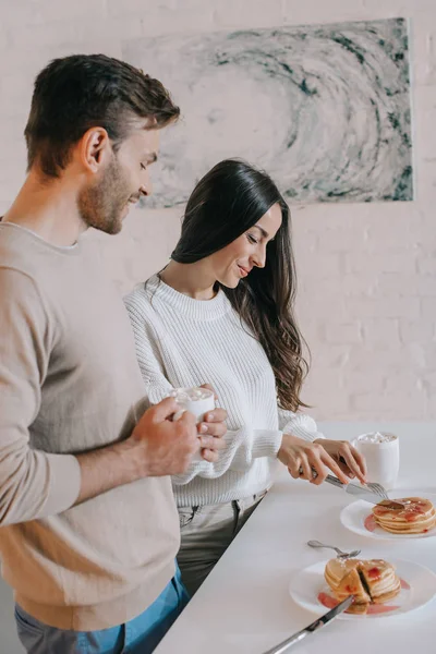 Belo jovem casal com panquecas para o café da manhã em casa — Fotografia de Stock