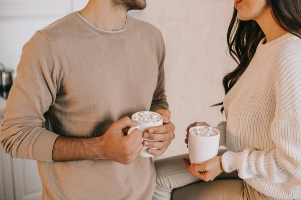 Cropped shot of young couple holding mugs of cocoa with marshmallow — Stock Photo
