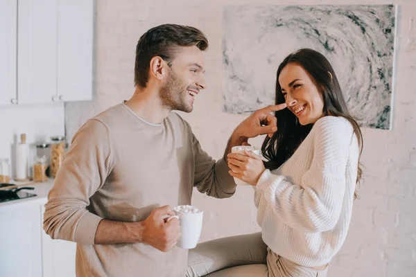 Glückliches junges Paar kuschelt mit Kakao und Pfannkuchen in der Küche — Stockfoto