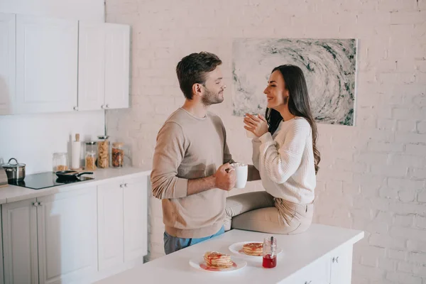 Улыбающаяся молодая пара завтракает вместе и болтает дома — стоковое фото