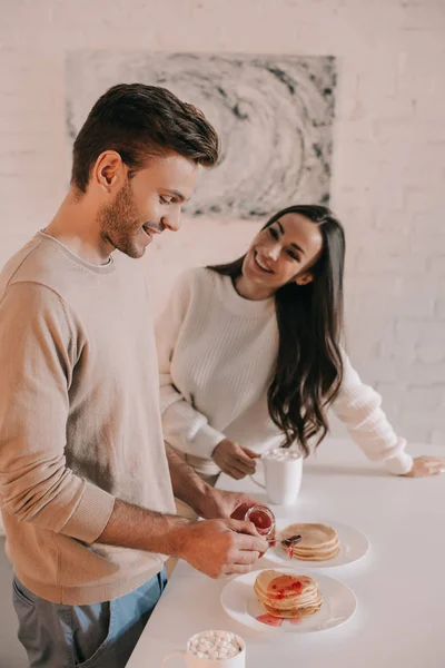 Hermosa pareja joven con panqueques con mermelada para el desayuno en casa - foto de stock