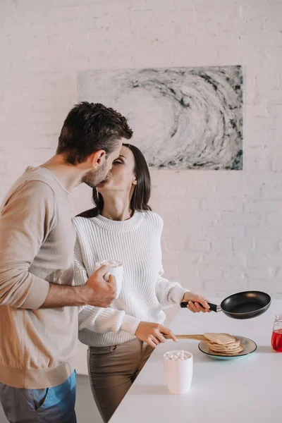 Beautiful young couple making breakfast together and kissing — Stock Photo