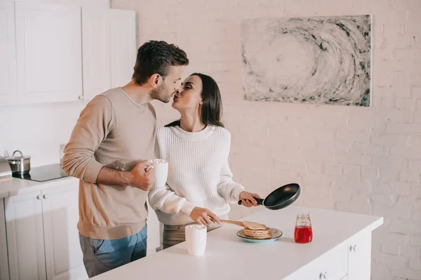 Happy young couple making breakfast together and kissing — Stock Photo