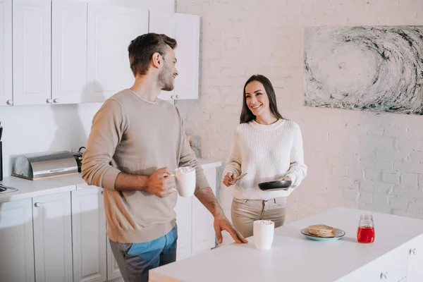 Lächelndes junges Paar macht leckere Pfannkuchen zum gemeinsamen Frühstück zu Hause — Stockfoto