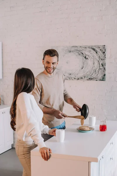 Happy young couple making delicious pancakes for breakfast together at home — Stock Photo