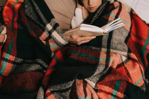 Cropped shot of young couple reading book together on couch under plaid at home — Stock Photo