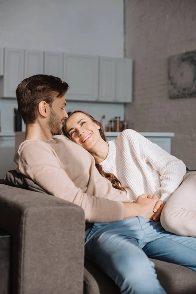 Sonriente romántico joven pareja coqueteando en sofá en casa - foto de stock