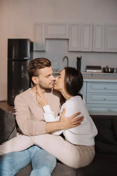 Romántico joven pareja besos en sofá en casa - foto de stock