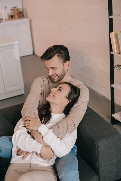 Vue grand angle de jeune couple souriant embrassant sur le canapé à la maison — Photo de stock