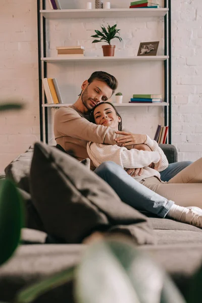 Bella giovane coppia che abbraccia sul divano a casa — Foto stock