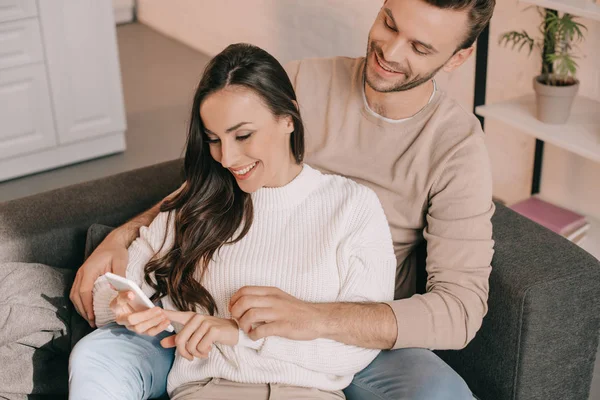 Высокий угол зрения счастливой молодой пары с помощью смартфона вместе на диване дома — стоковое фото